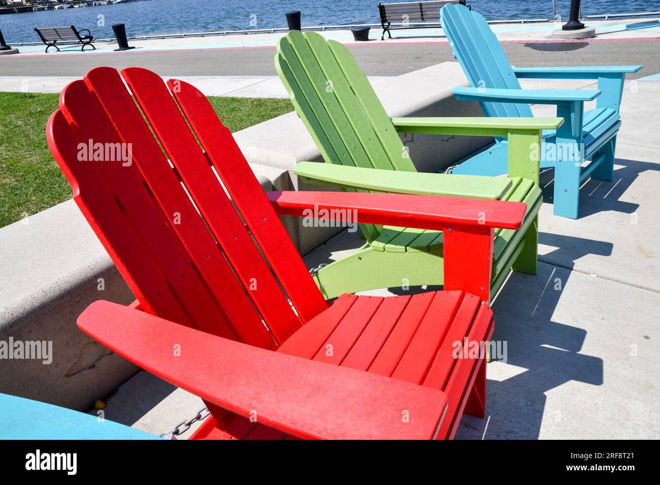 Fila di sedie vuote colorate per prato Adirondack lungo la parete del porto Foto Stock