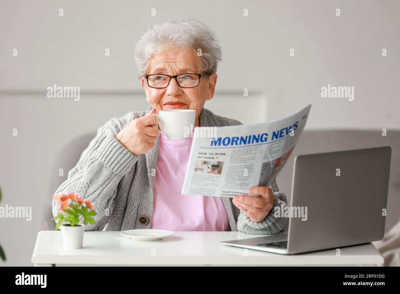 Donna anziana con giornale che beve caffè a casa Foto Stock