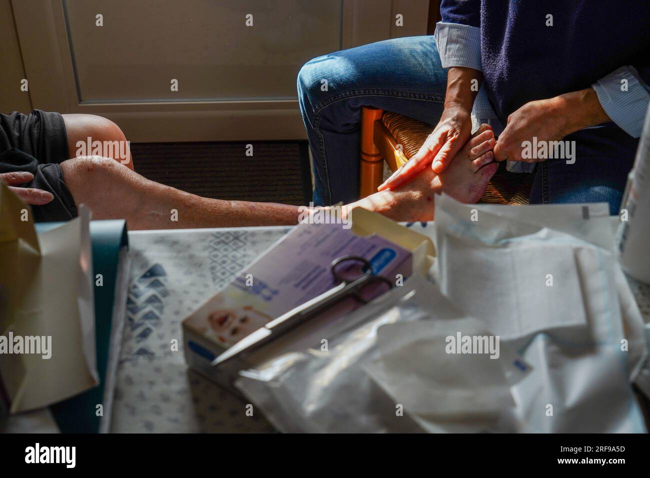 Infermiera freelance durante la sua visita quotidiana a una persona anziana. Cura delle gambe. Foto Stock