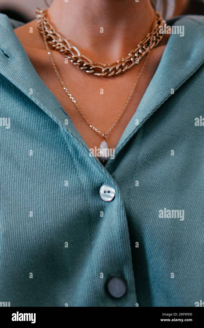 Dettaglio ravvicinato di una blusa femminile blu e collana con catena dorata. Accessori alla moda. Shot verticale Foto Stock