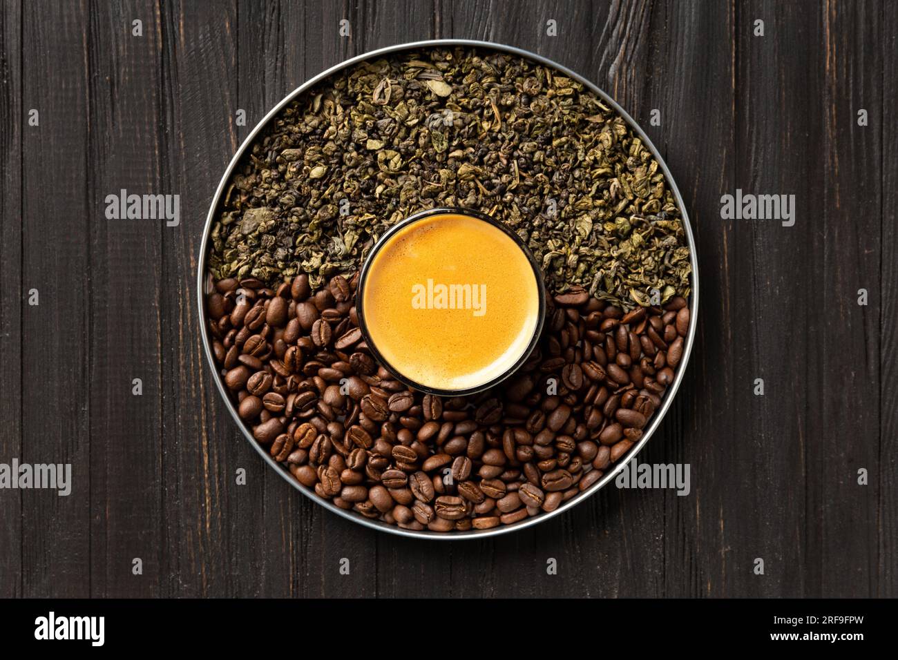 Composizione di foglie di tè verde secco, chicchi di caffè tostati in una scatola rotonda e caffè in una tazza su uno sfondo di legno scuro vista dall'alto. Foto Stock