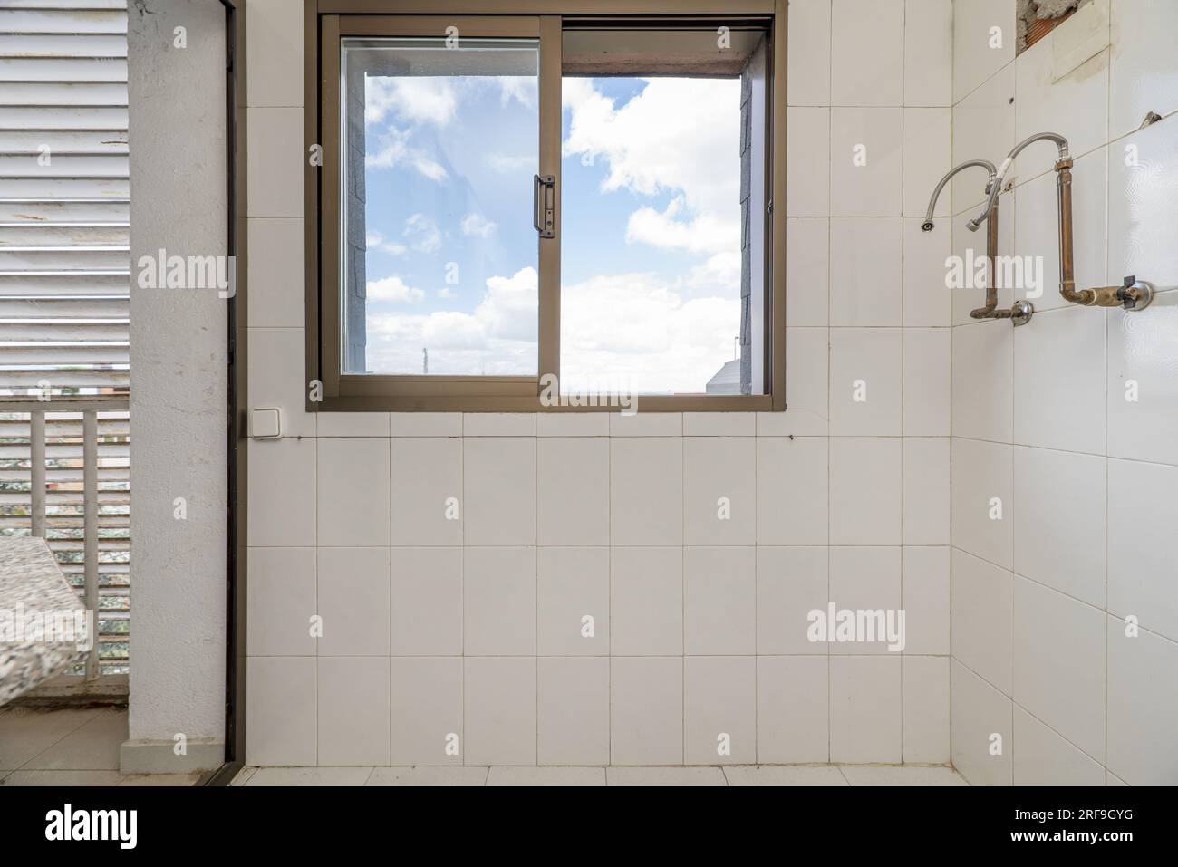 Parete vuota di una cucina usata con una finestra e alcuni tubi di una caldaia a gas smontata Foto Stock