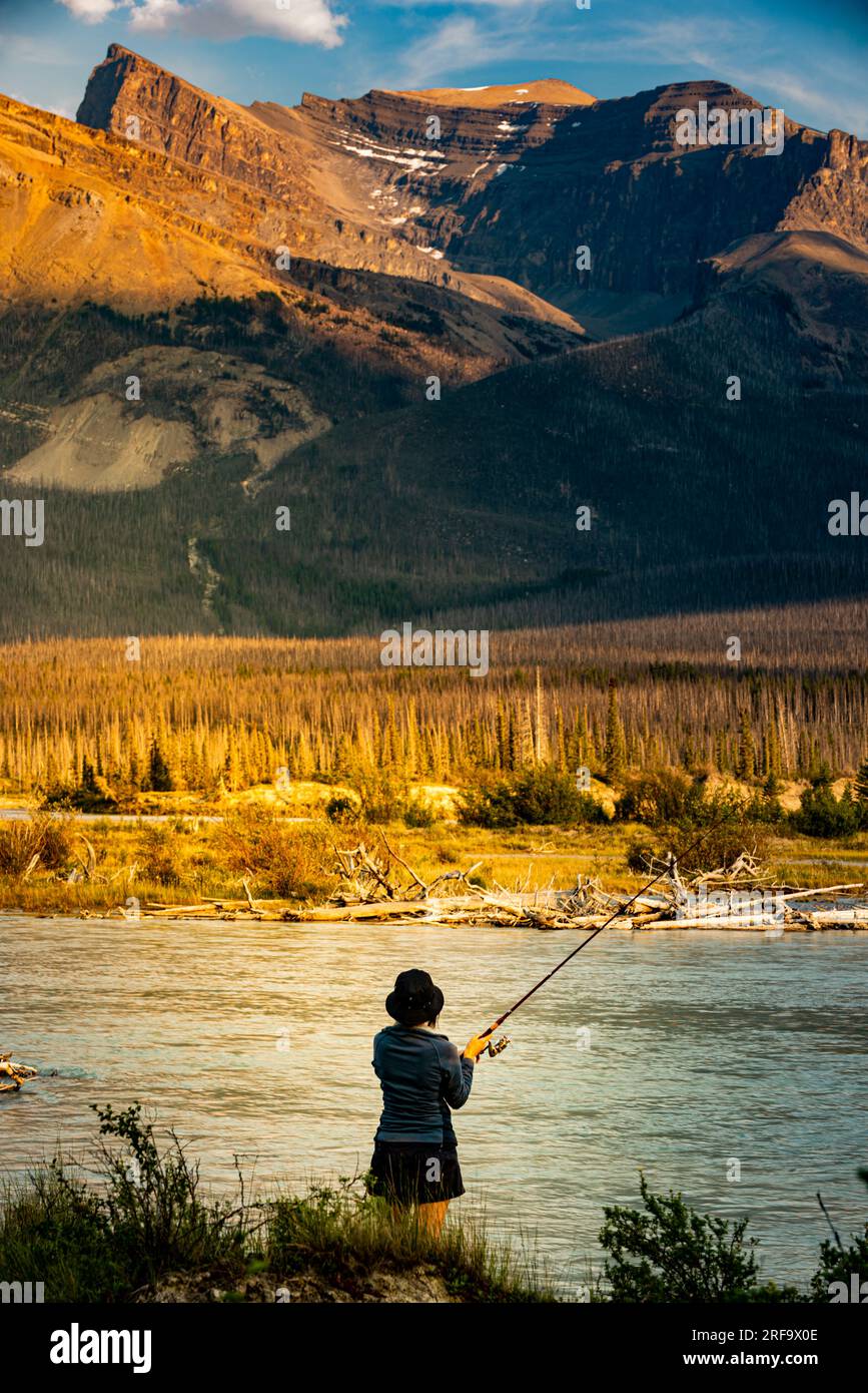 Una donna che pesca nel North Saskatchewan River, Canada, in Alberta, circondata da una natura selvaggia mozzafiato, che si gode la bellezza della natura e l'emozione di pescare Foto Stock