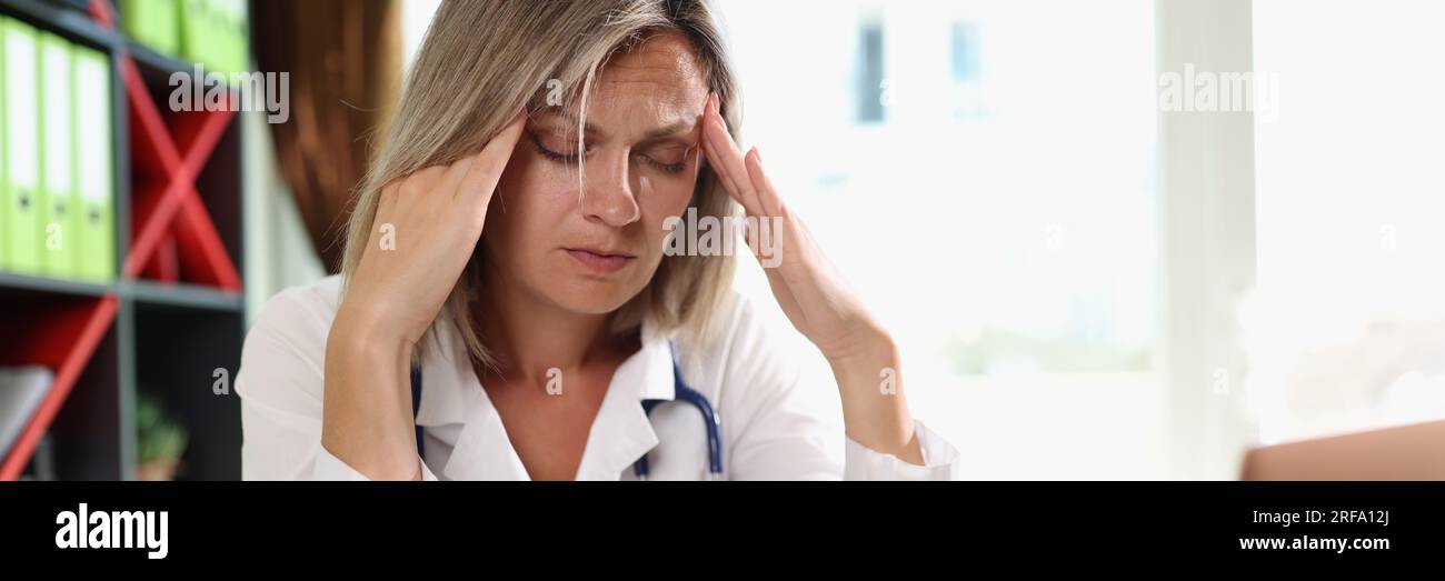 Medico di sesso femminile esausto che ha mal di testa durante il lavoro in clinica. Foto Stock