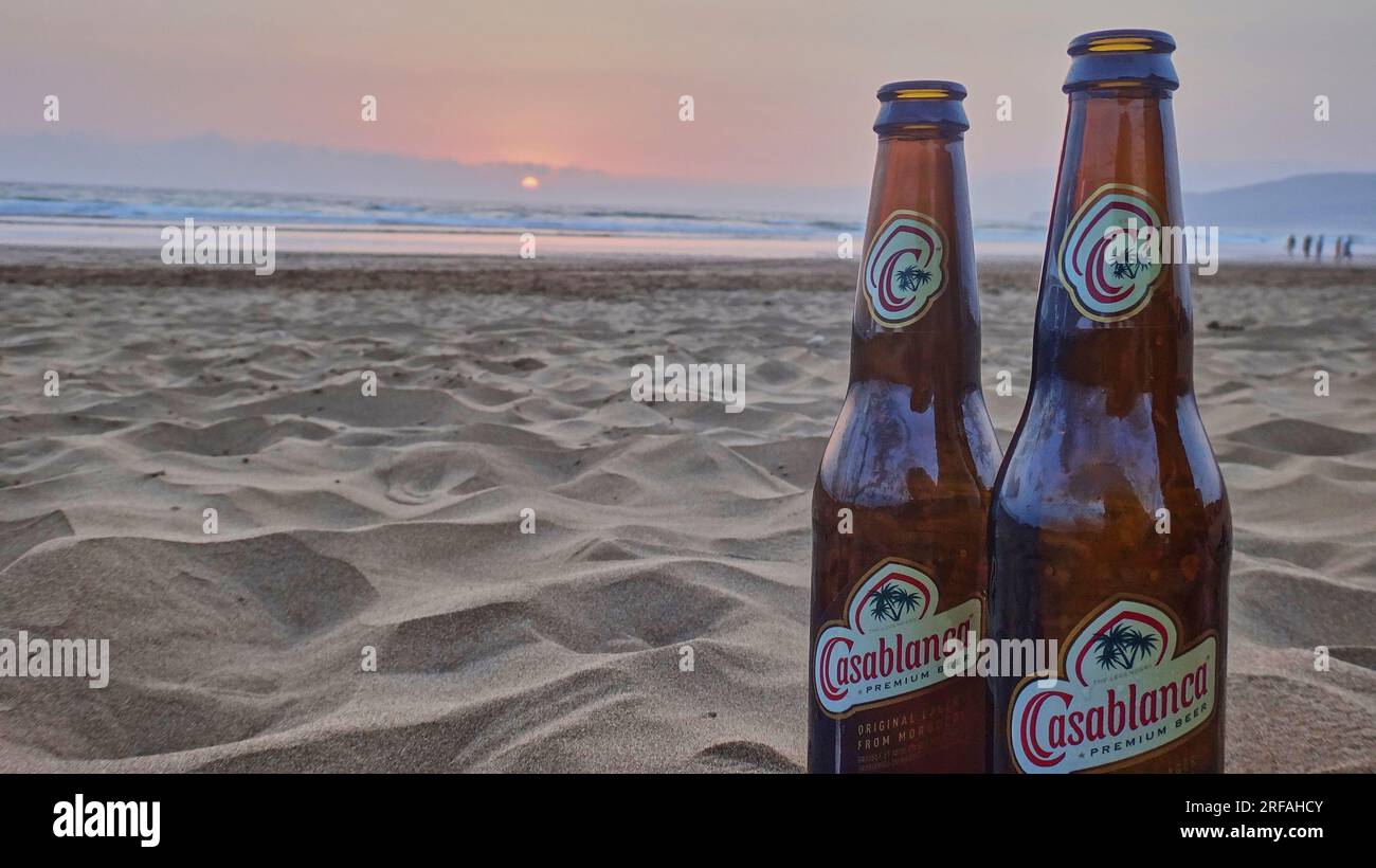 Casablanca, Marocco - 05 19 2016: Bottiglia di birra di Casablanca in piedi su una spiaggia di sabbia di fronte a un romantico tramonto sull'oceano atlantico. Foto Stock