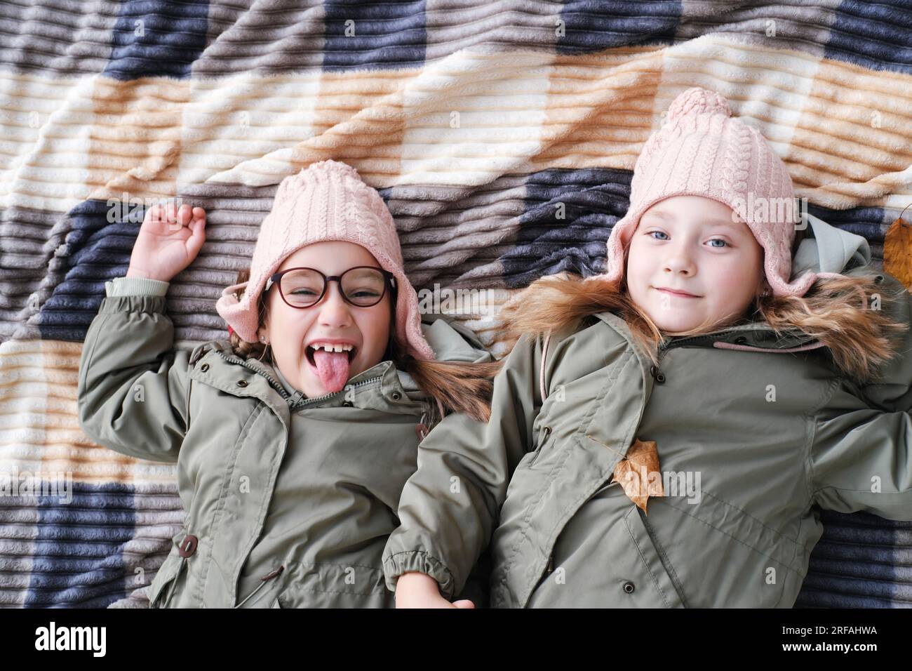 Due sorelle gemelle felici giacciono su una coperta in un parco autunnale. Le ragazze sorridono e guardano la telecamera, una delle sorelle si sta prendendo gioco e s Foto Stock
