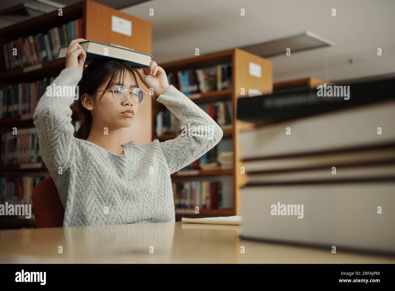 Studentessa asiatica leggeva libri in biblioteca all'università. La giovane ragazza stanca dello stress ha un problema mentre studia duramente. Concetto di tristezza Foto Stock