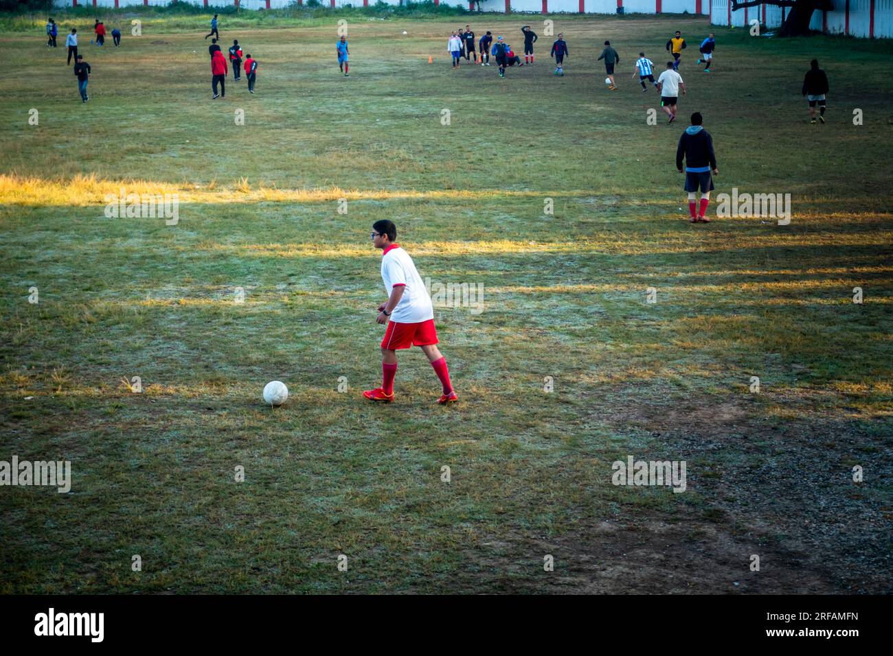 14 ottobre 2022 Uttarakhand, India. Giovane giocatore di calcio dilettante in pantaloncini rossi che tira un tiro su un campo di calcio a Uttarakhand, India. Passione per il Foto Stock
