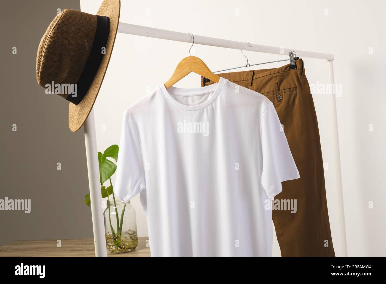 T-shirt bianca, cappello e pantaloni marroni appesi alla barra appendiabiti con spazio per le copie su sfondo bianco Foto Stock