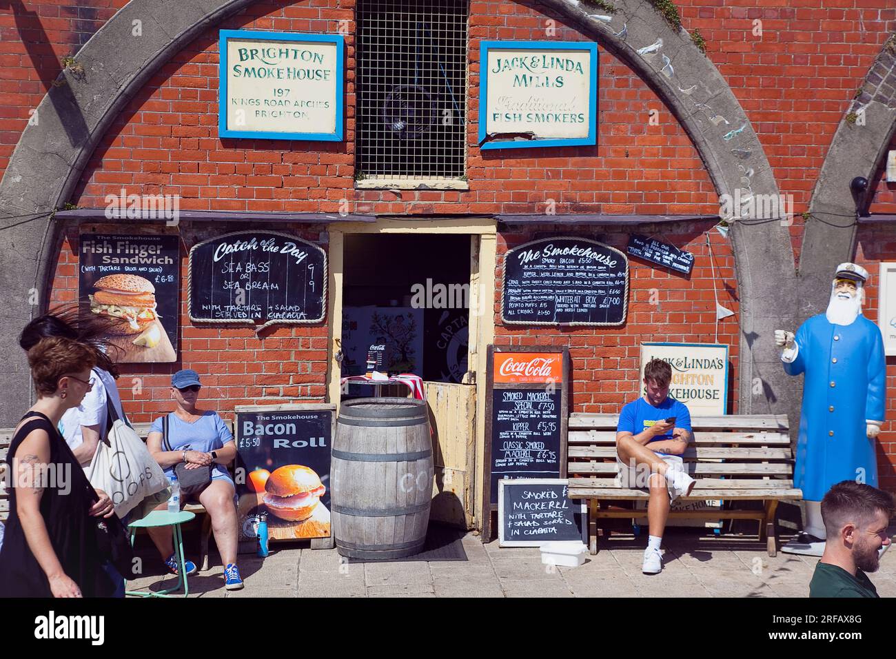 Inghilterra, East Sussex, Brighton, venditore di panini di pesce Smokehouse ad arco lungo il lungomare, affollato di turisti estivi. Foto Stock