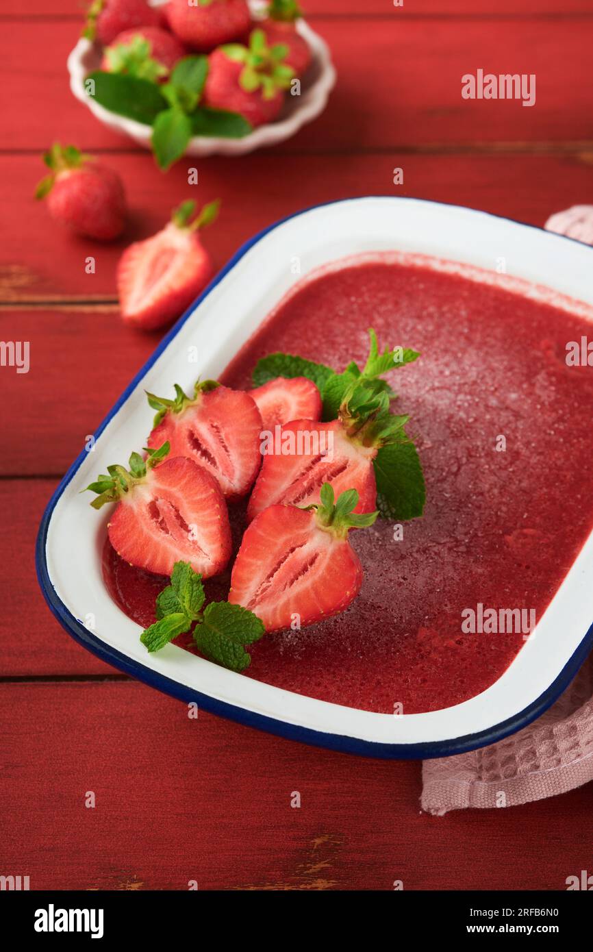 Granita di fragole o sorbetto di bacche fresche in un recipiente rustico bianco su un vecchio fondo di legno. Gelato con fragole e menta. Delizia estiva. vi superiore Foto Stock