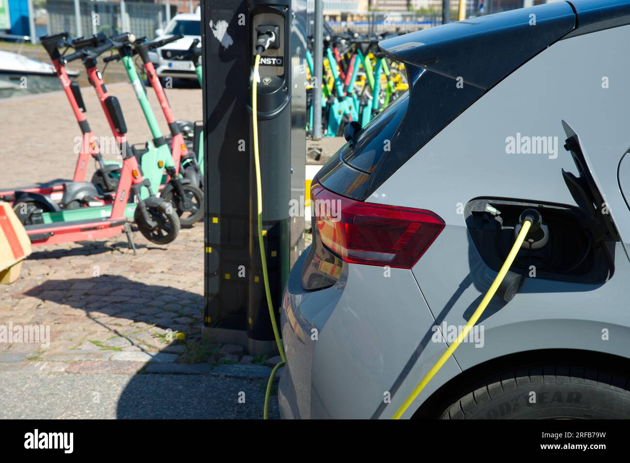 L'auto Elesctri viene ricaricata di fronte agli scooter elettrici di Helsinki, Finlandia Foto Stock