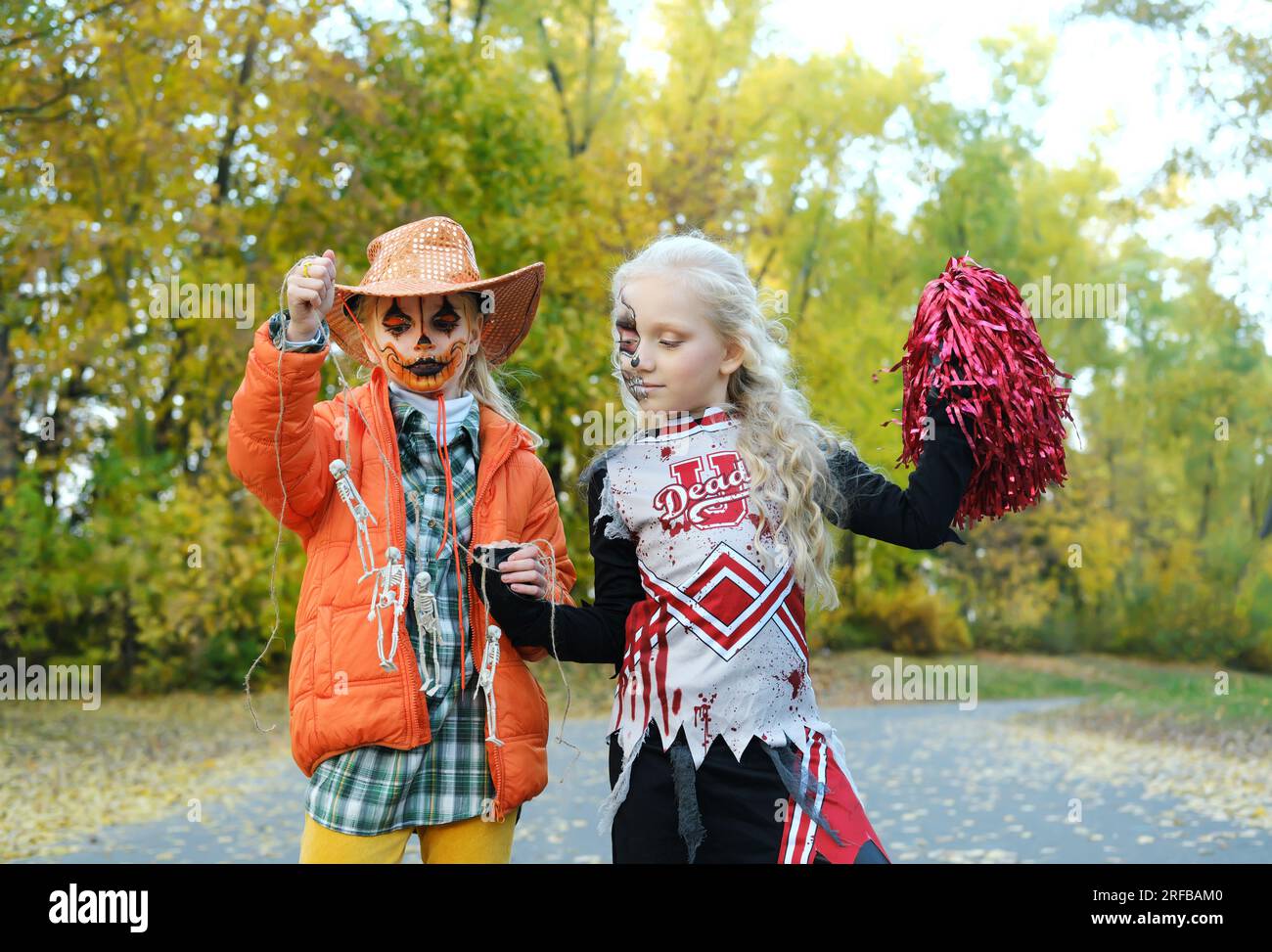 Bambina con una giacca arancione e un cappello da cowboy mostra alla sua amica in costume da cheerleader i suoi scheletri su una corda. Festa di Halloween. P orizzontale Foto stock