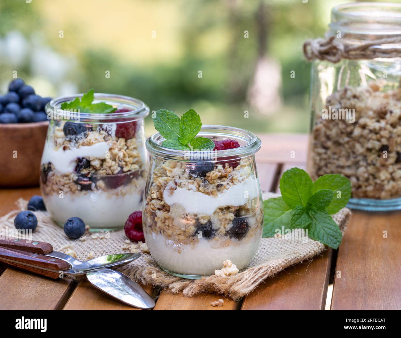 Parfait di yogurt con muesli, mirtilli e lamponi guarniti con menta all'aperto su un tavolo da patio in legno Foto Stock