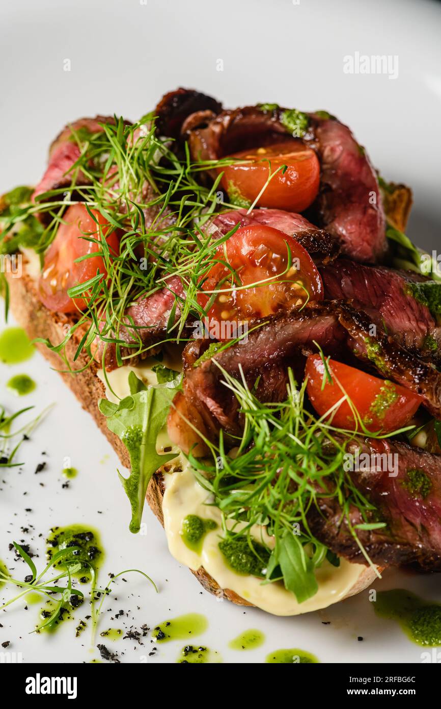 Bruschetta con succosa carne, pomodori, erbe, formaggio, salsa al pesto su un piatto bianco. Primo piano. Foto Stock