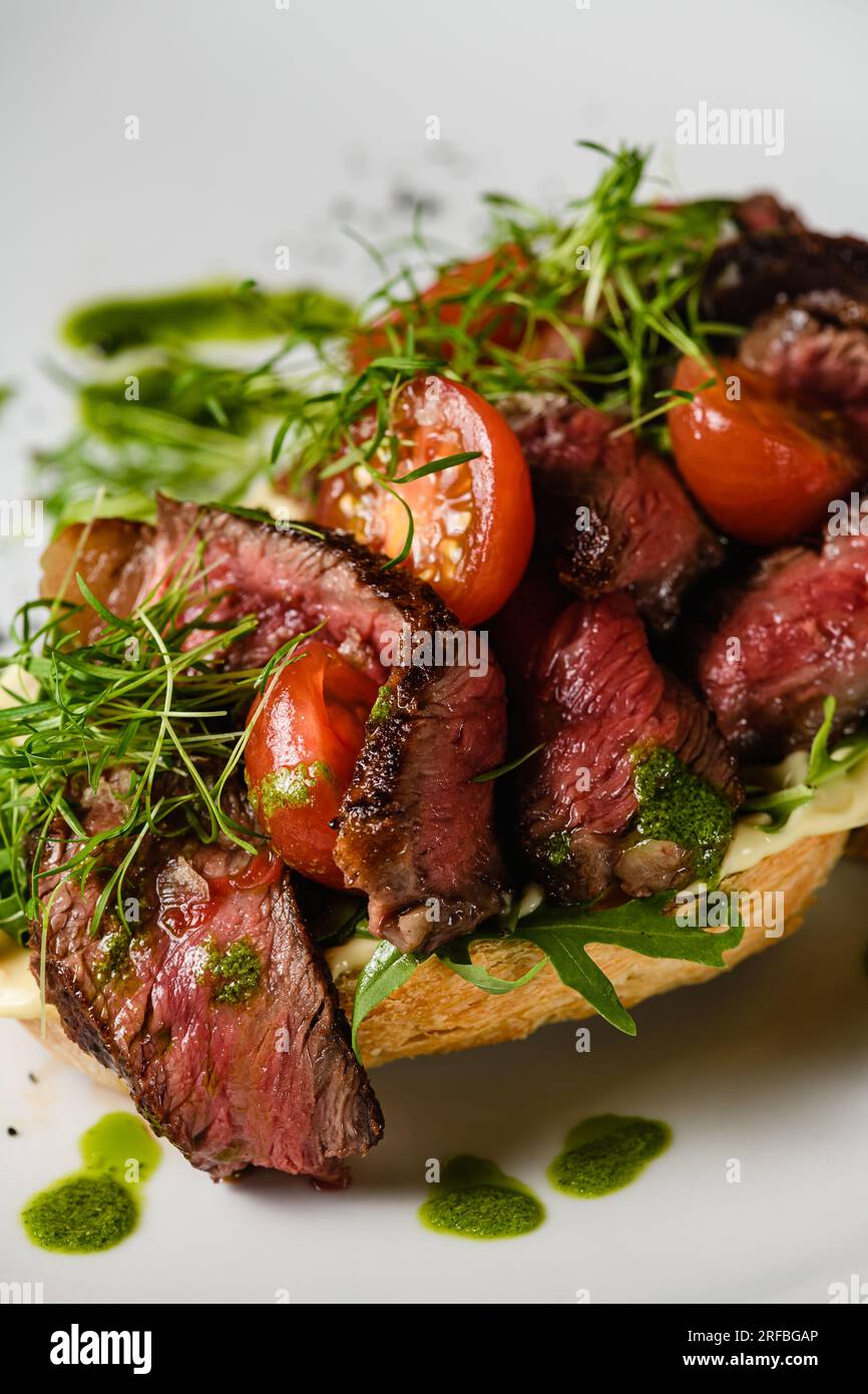 Bruschetta con succosa carne, pomodori, erbe, formaggio, salsa al pesto su un piatto bianco. Primo piano. Foto Stock