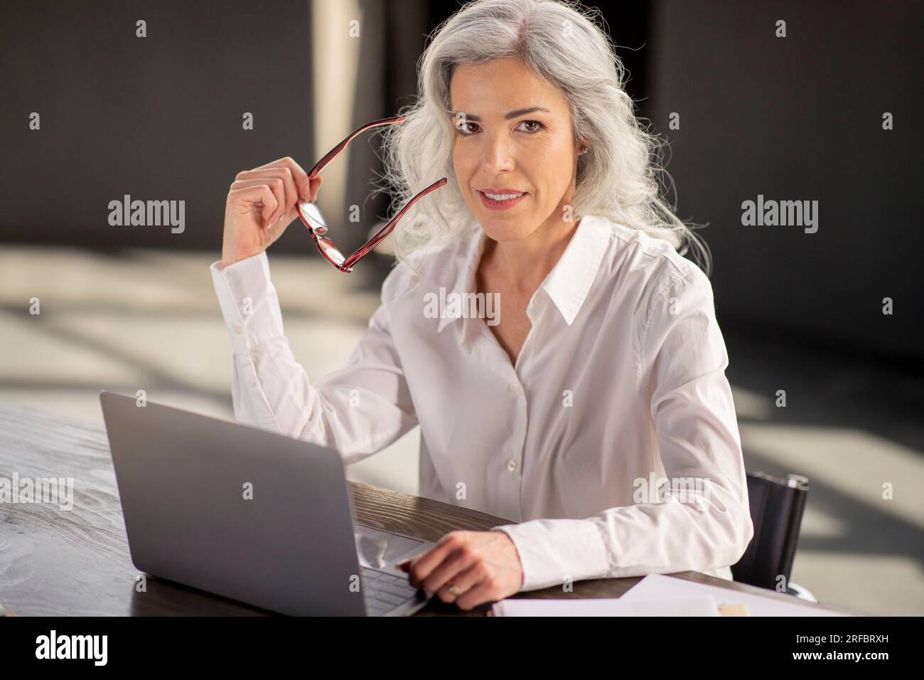 Donna d'affari in posa con occhiali da vista seduti con un notebook in un ufficio moderno Foto Stock