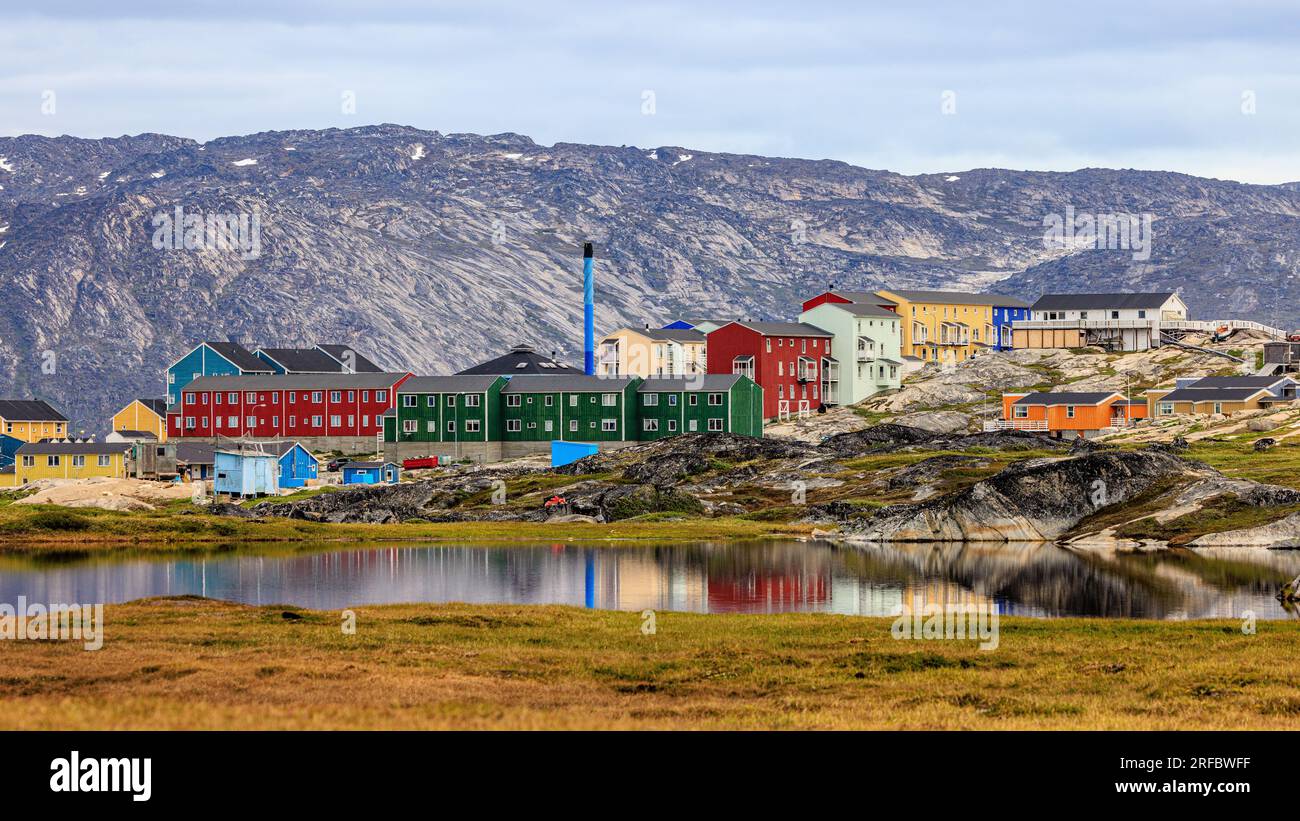 le case colorate di ilulissat si riflettono in uno stagno ancora con uno sfondo montuoso Foto Stock