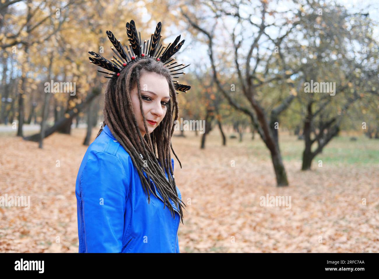 Una donna di mezza età in dreadlocks e un cerchio sui capelli in piume cammina nel parco autunnale. La donna sta guardando la telecamera. Foto orizzontale Foto Stock