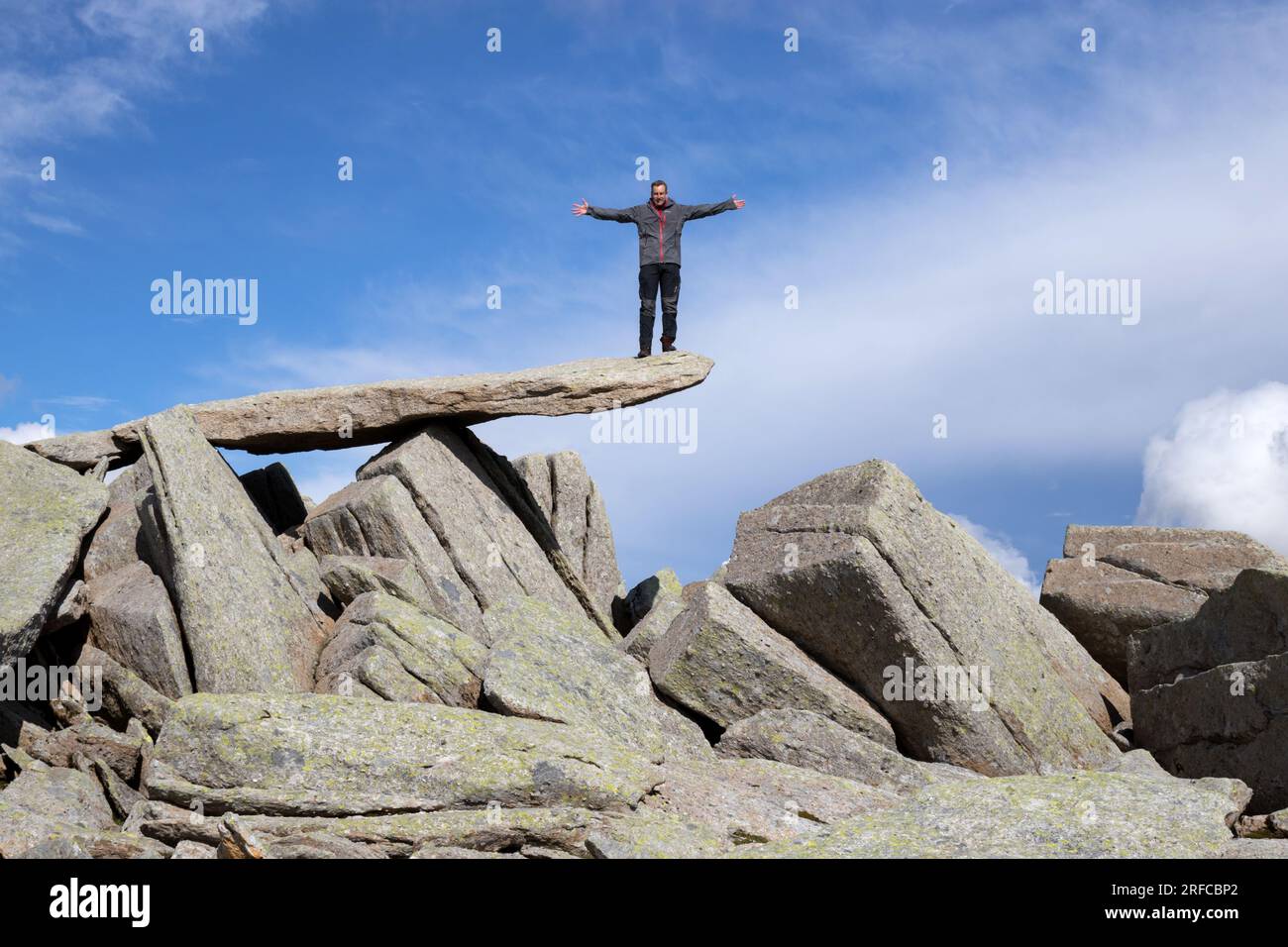 Bilanciare la roccia sulla cima di Glyder Fach con una persona in piedi sulla cima. Foto Stock