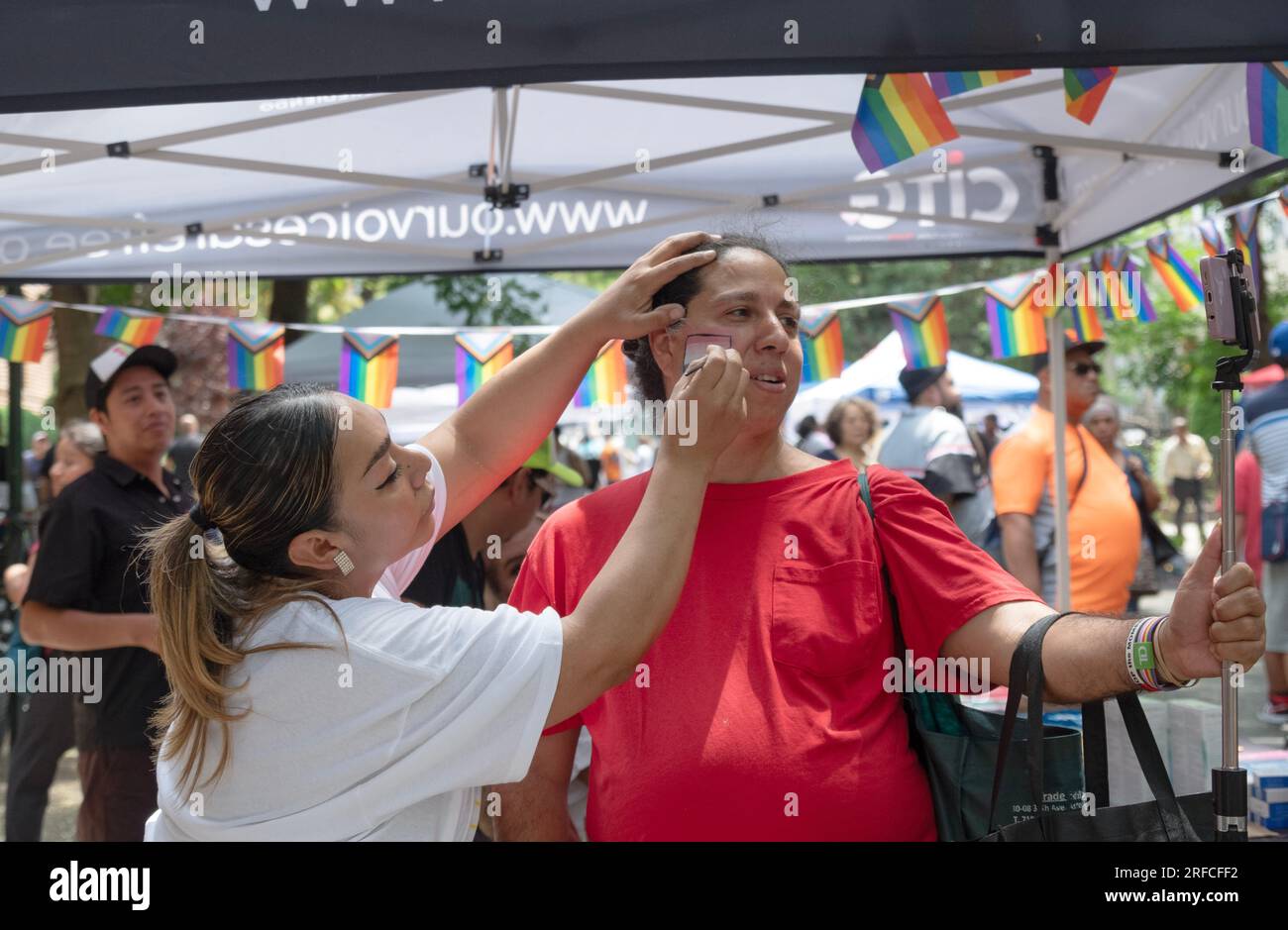 Al Transfest una trans fa un selfie mentre la bandiera trans le viene dipinta sulla guancia. A Jackson Heights, Queens, New York. Foto Stock