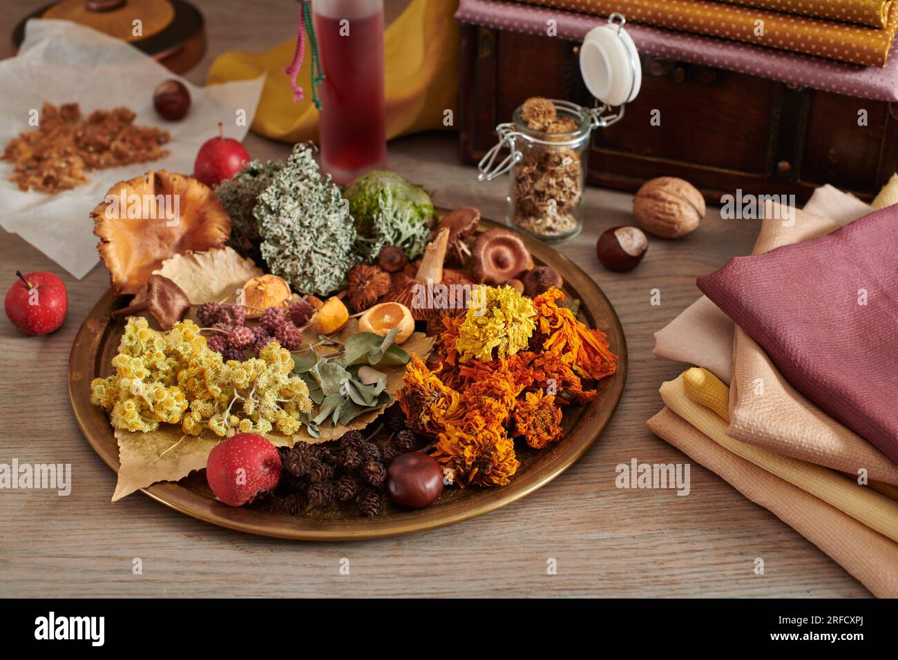 Materiale vegetale per la tintura organica di tessuti su un piatto, pila di tessuti tinti a mano sullo sfondo petto di legno con tessuti Foto Stock