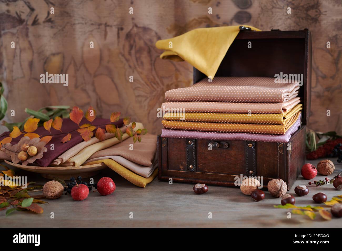 Cassa in legno e piatto in legno con pile di tessuti tinti a mano, foglie autunnali, noci e frutti di bosco su sfondo eco-stampato Foto Stock