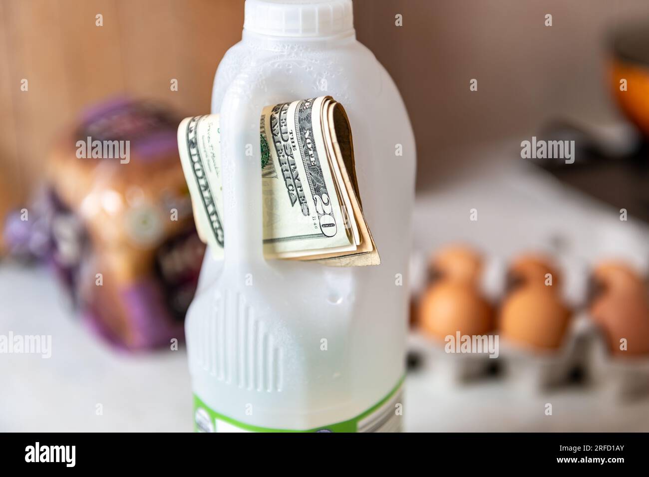 Costo della vita, concetto di inflazione alimentare con un pacchetto di bollette da dollari americani incastonate nella maniglia di una bottiglia di latte. Foto Stock