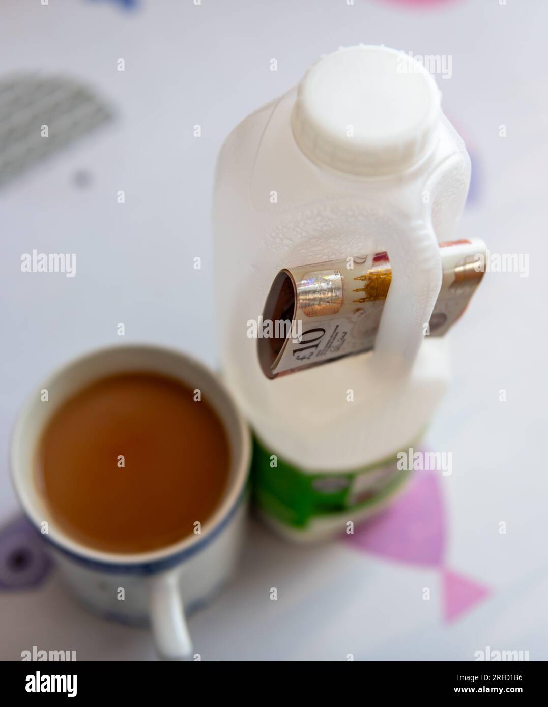 Costo della vita, concetto di inflazione alimentare con un pacchetto di banconote da sterlina incastonate nella maniglia di una bottiglia di latte con una tazza di tè. Foto Stock