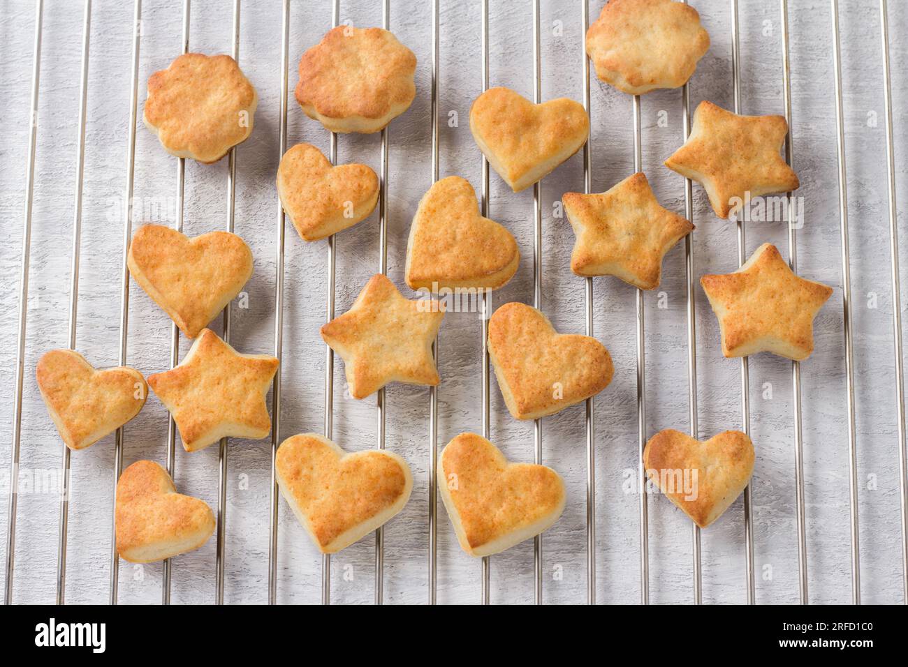 Biscotti al formaggio cottage appena sfornati a forma di stelle e cuori su una griglia d'acciaio, vista dall'alto. Fase di cottura di deliziosi biscotti fatti in casa. Foto Stock