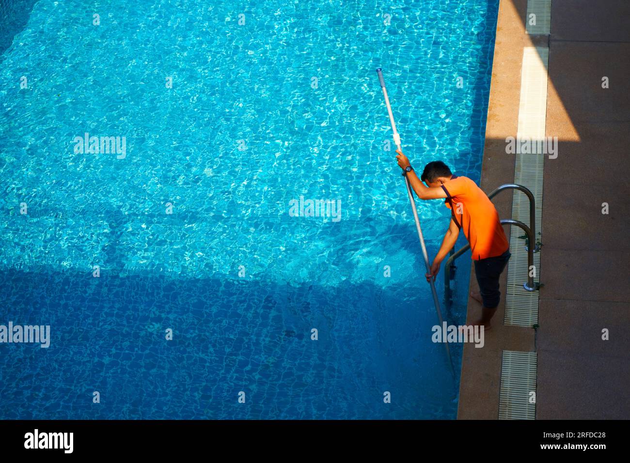 Vista dall'alto di un lavoratore che pulisce una piscina in una casa privata in estate. Foto Stock