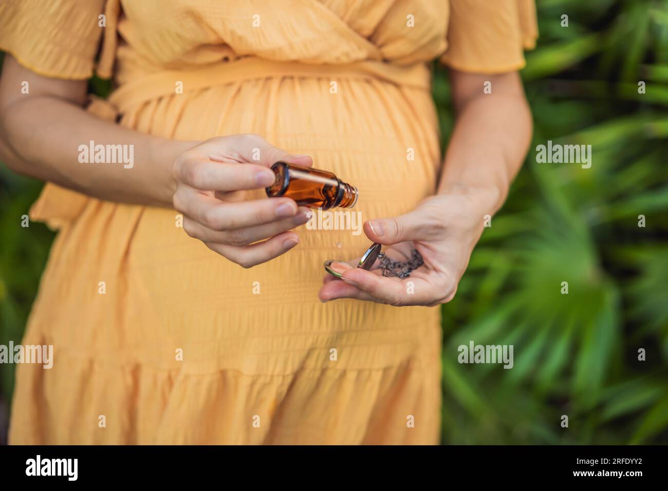 donna incinta dopo il 40 dimostrando l'uso di un ciondolo aromatico, combinando stile e aromaterapia durante il suo viaggio di gravidanza Foto Stock