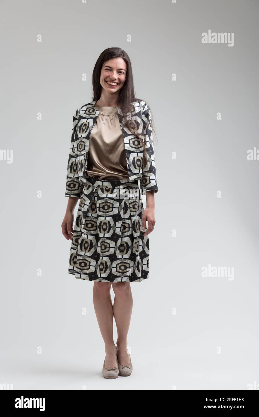 Modello alla moda con carnagione leggera e occhi, in posa con abiti fantasia anni '70, gonna lunga al ginocchio e tacchi medi beige. Piena di gioia, che mostra beaut Foto Stock