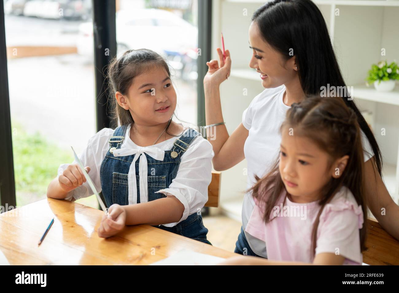 Una graziosa giovane ragazza asiatica che si diverte a studiare con un insegnante privato, prendendo una lezione supplementare a casa. Bambini dell'asilo, studen della scuola elementare Foto Stock