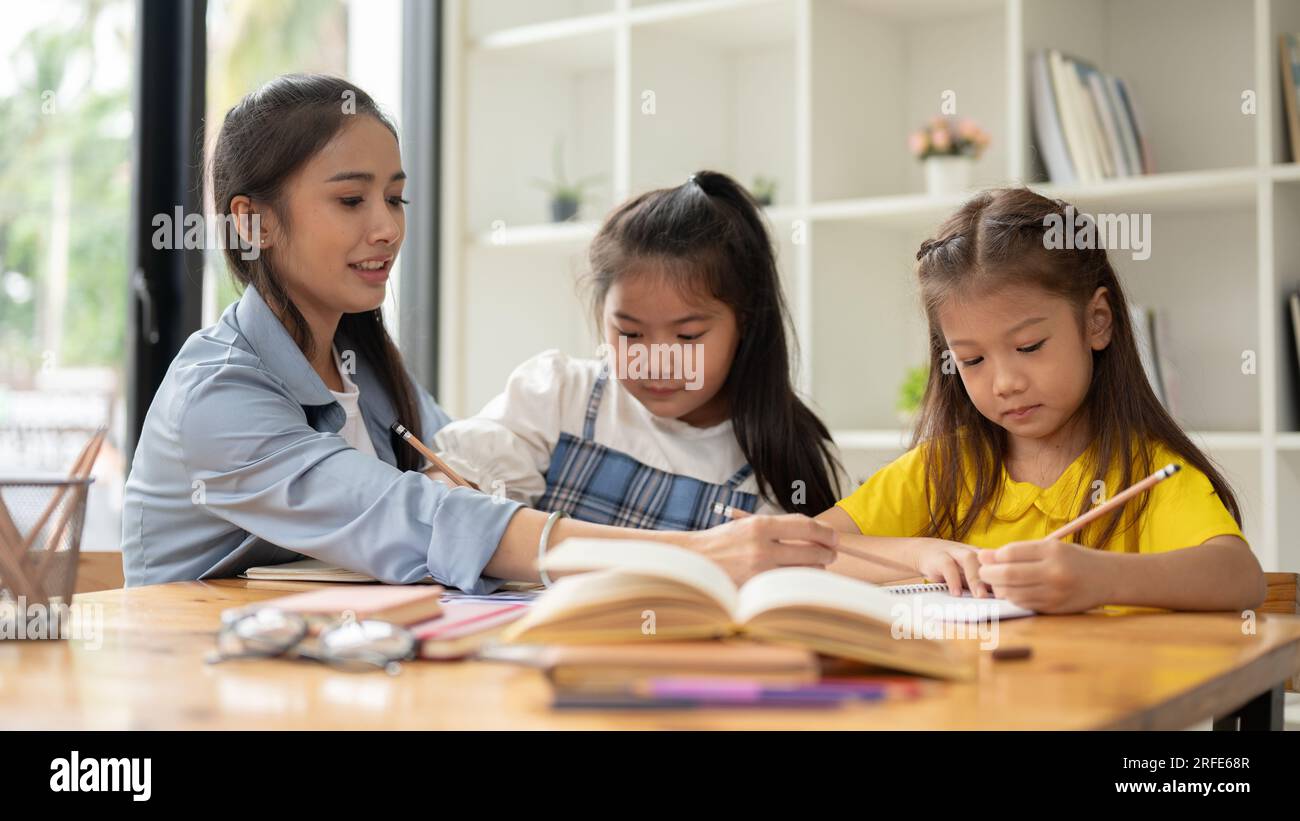 Due graziose bambine asiatiche si concentrano sullo studio e sul fare i compiti con un insegnante privato a casa. bambini, bambini, scuola materna, scuola materna Foto Stock