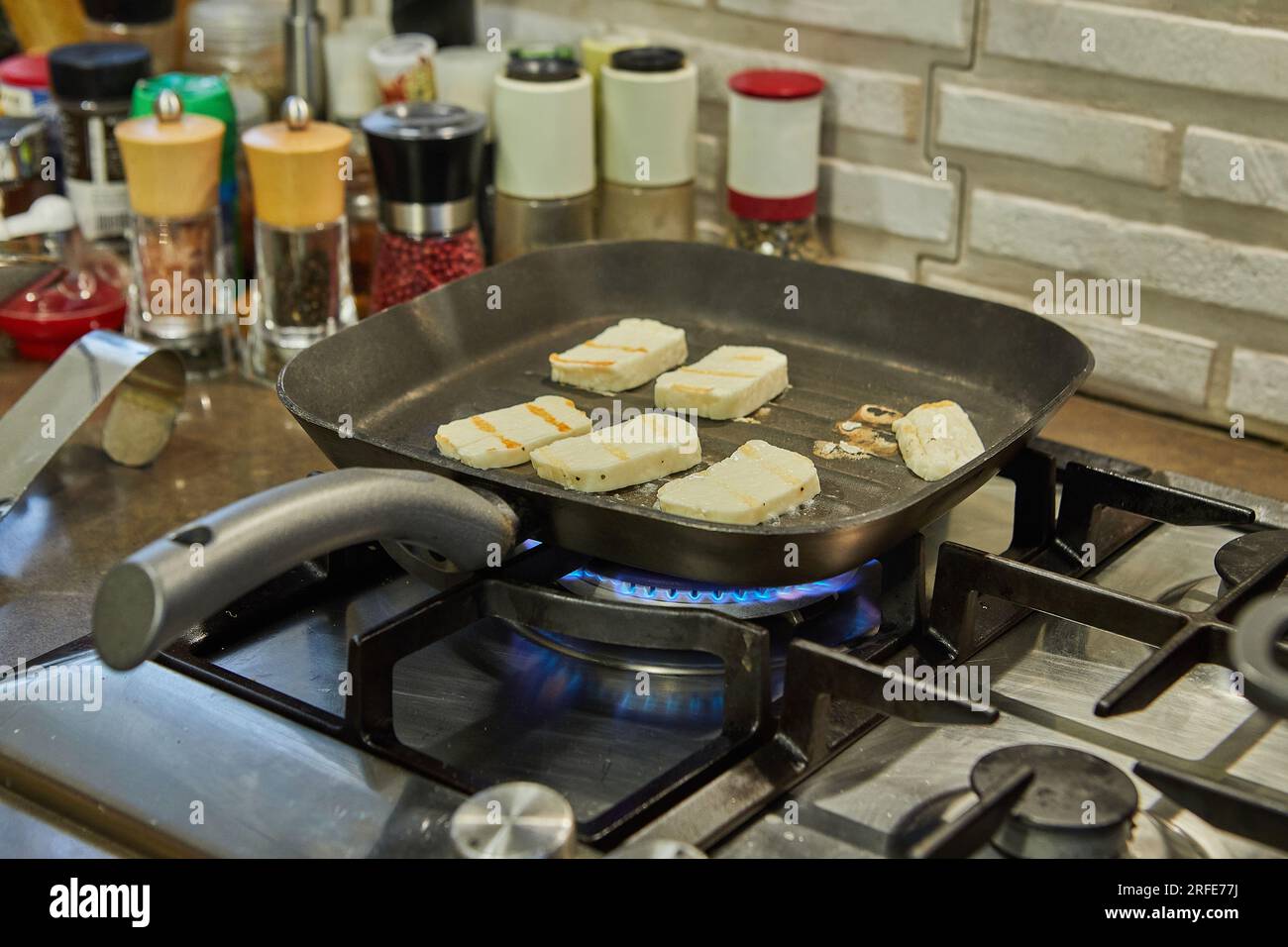 Il formaggio halloumi viene fritto su una teglia a coste sul fuoco sulla stufa a gas. Foto Stock