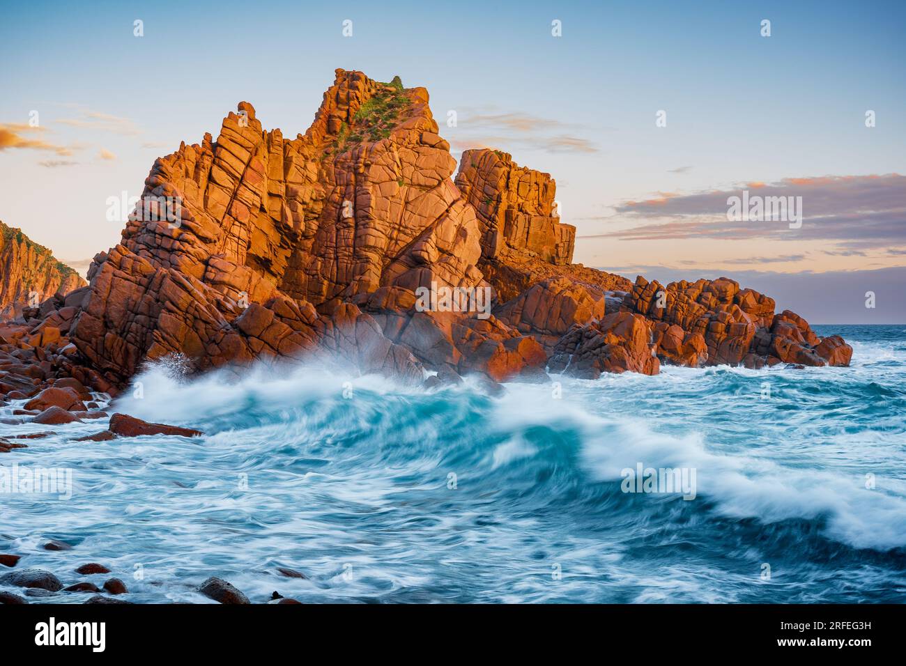 Grandi onde che si infrangono contro formazioni rocciose costiere colorate dalla luce dorata della sera a Cape Woolamai, Phillip Island, Victoria, Australia Foto Stock