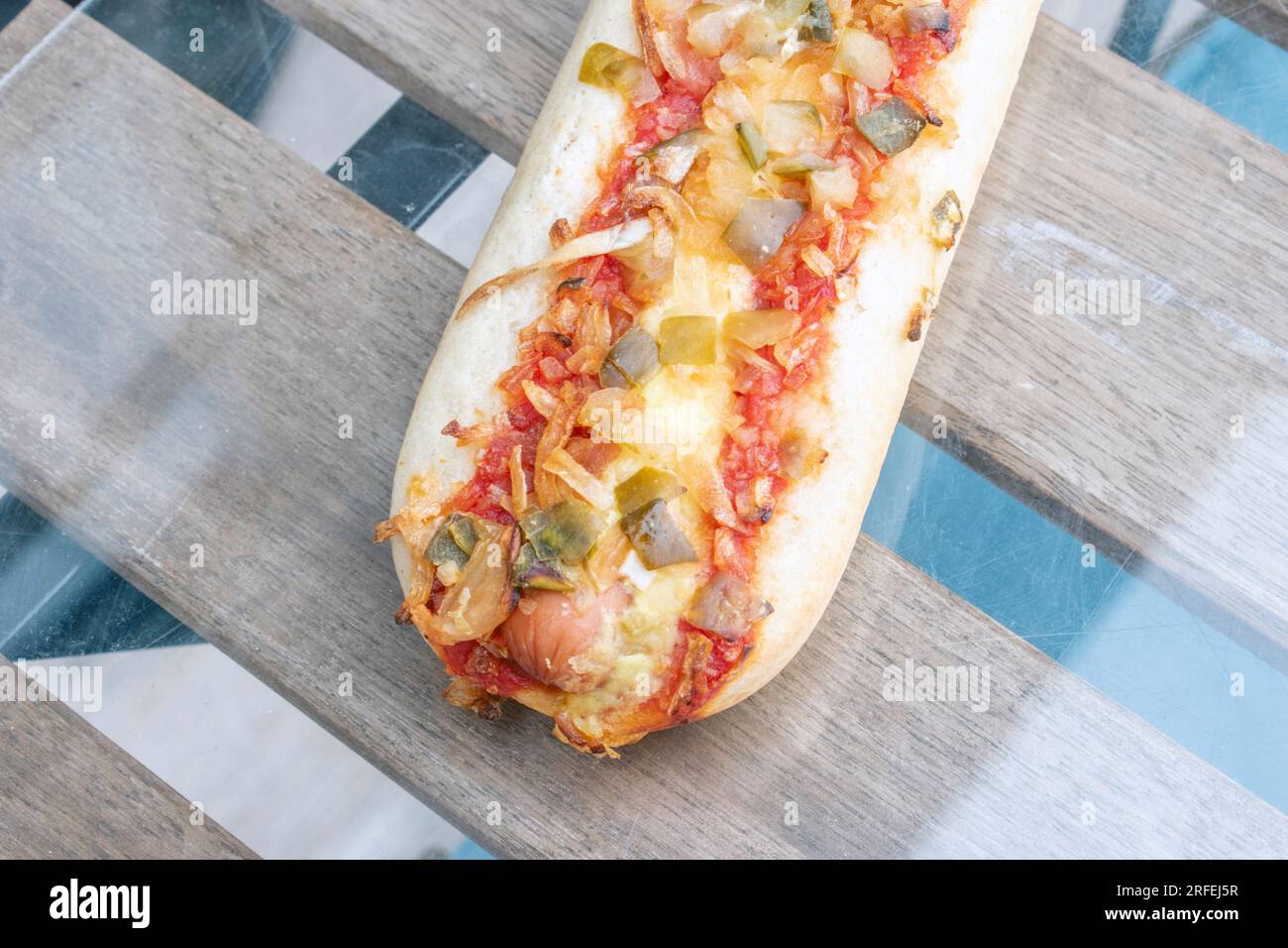 Hot Dog: Un delizioso hot dog pieno di gustosi sottaceti, cipolle fritte e un pizzico di salsa di pomodoro, scattato in una foto appetitosa dall'alto su una g. Foto Stock