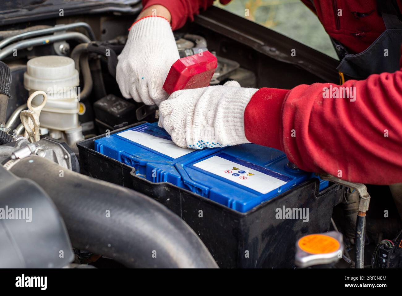 locksmith sostituisce la batteria dell'auto. Un uomo fissa i morsetti della batteria sotto il cofano di un'auto. Foto Stock