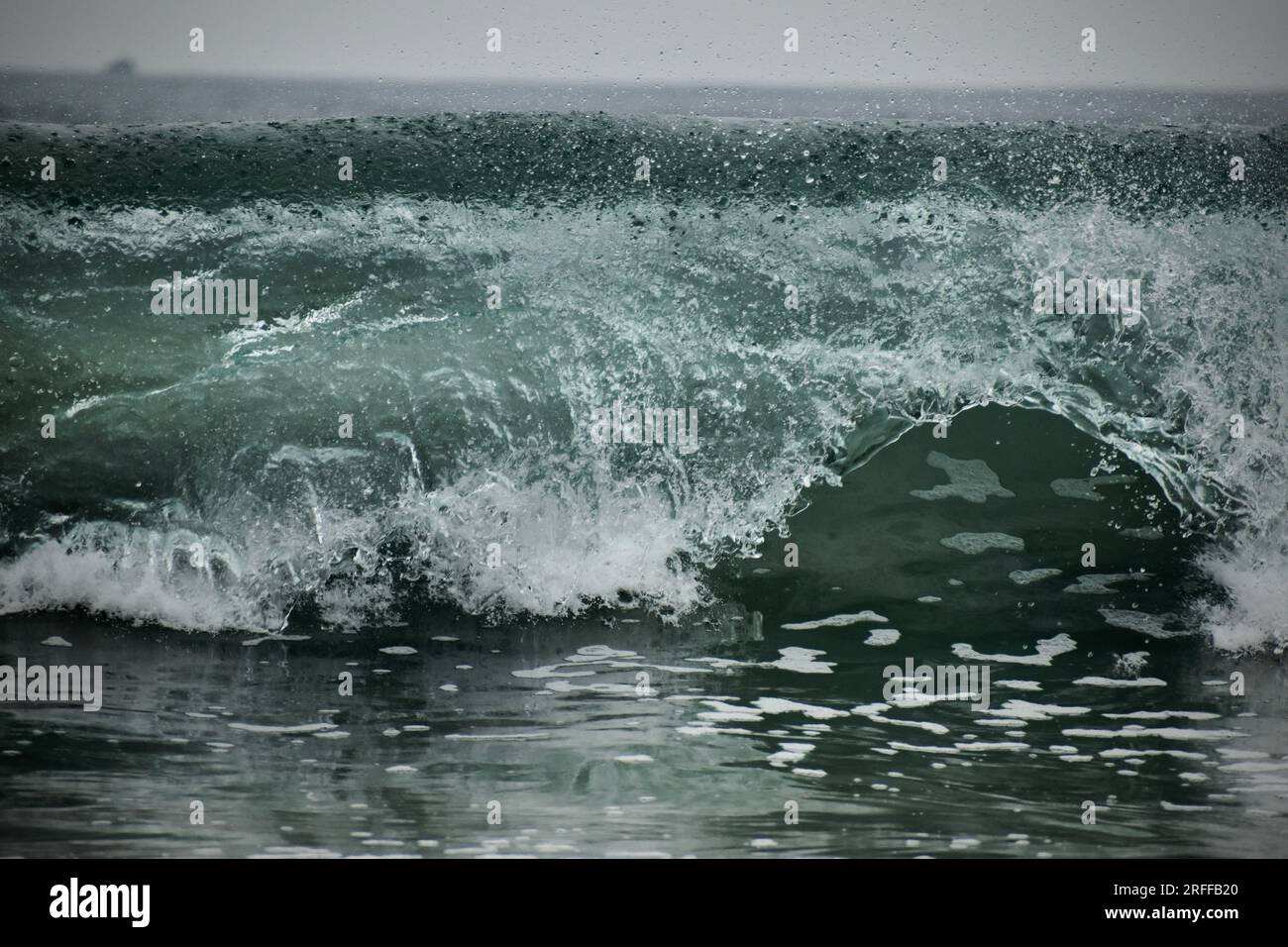 Onde oceaniche che crescono e schiudono con gocce d'acqua che volano mentre si dirigono verso la spiaggia di sabbia Foto Stock