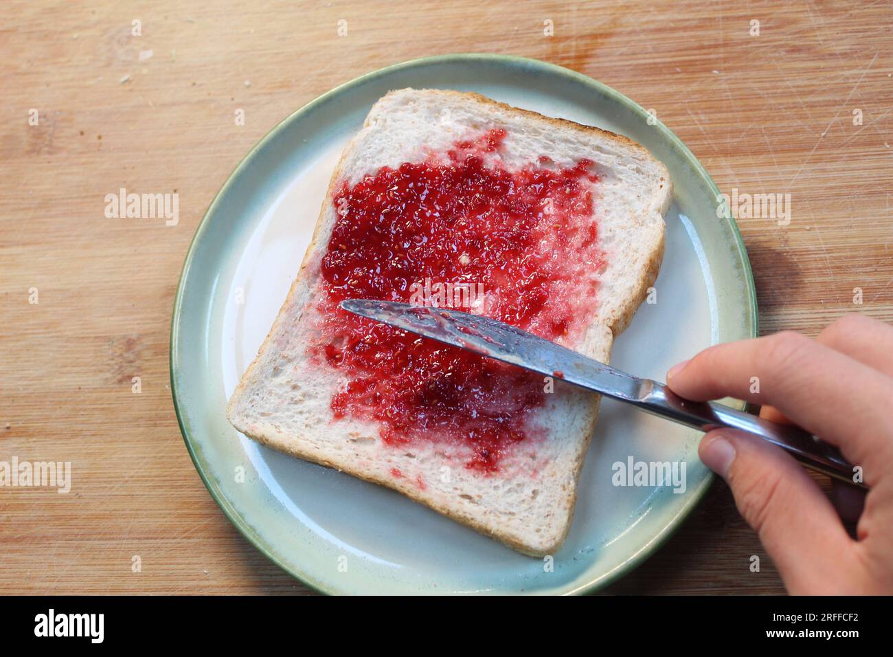 Una foto di qualcuno che distribuisce marmellata su un pezzo di pane bianco. Foto Stock