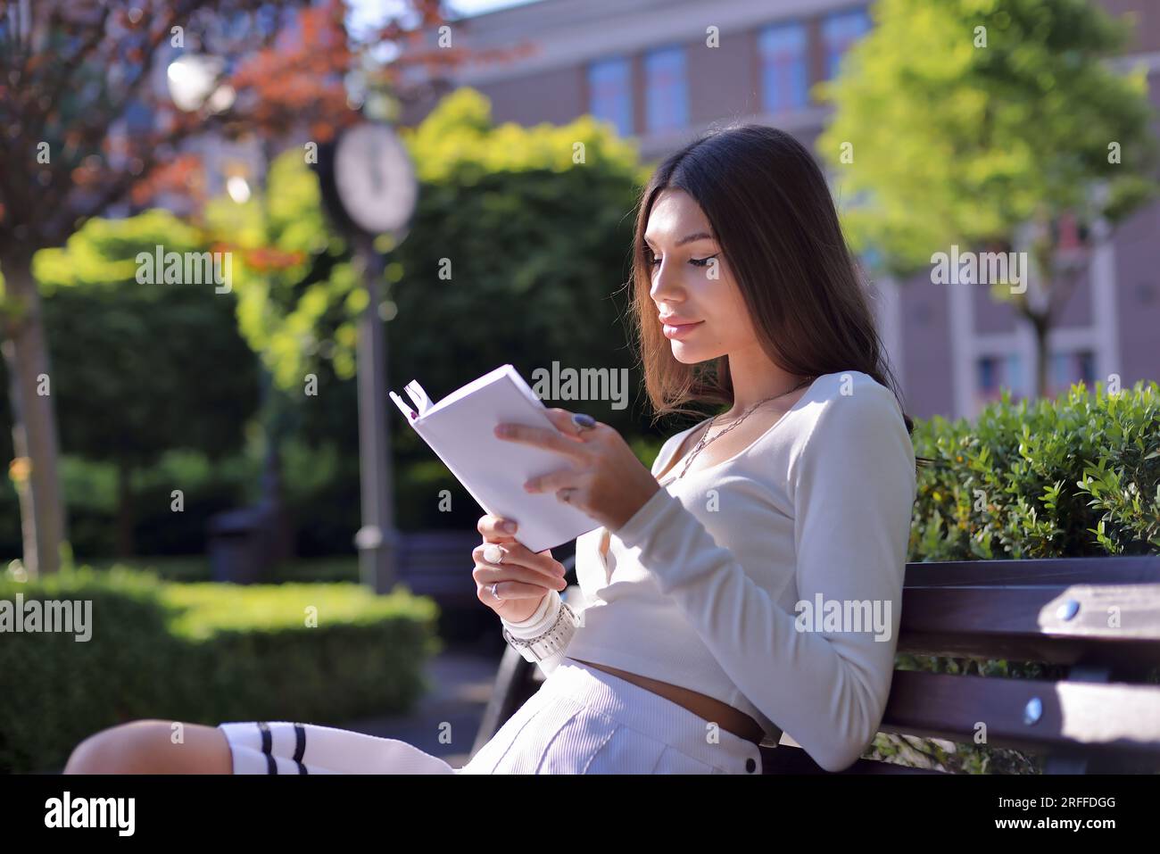 Felicità estiva: Donna che legge un libro all'aperto sulla panchina del parco. Abbracciando la natura, il bel tempo, l'abbigliamento informale, rilassato e gioioso Foto Stock