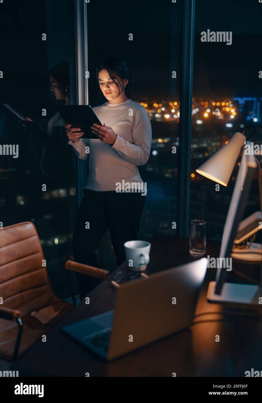 Donna d'affari caucasica dedicata che lavora a tarda notte nel suo ufficio, utilizzando un tablet digitale per analizzare i dati. Imprenditrice donna che legge un rapporto, m Foto Stock