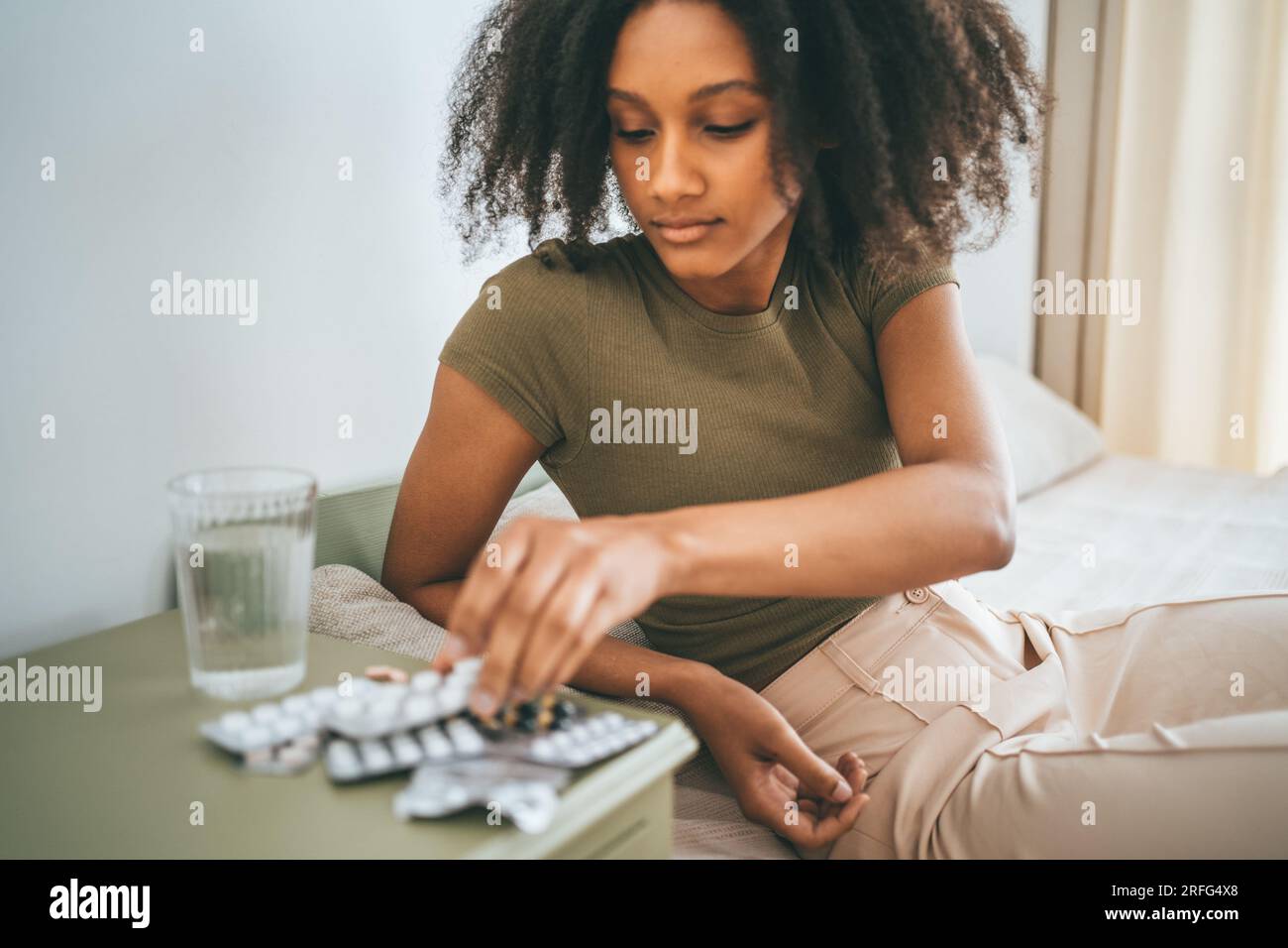 La ragazza afroamericana prende pillole o compresse dal tavolo. Farmaci, vitamine o integratori alimentari. Foto Stock