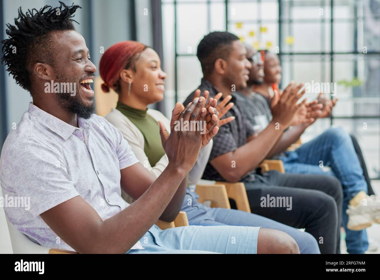 Un gruppo di uomini e donne siede di fila e applaude un uomo che fa un'idea o dice qualcosa. Foto Stock