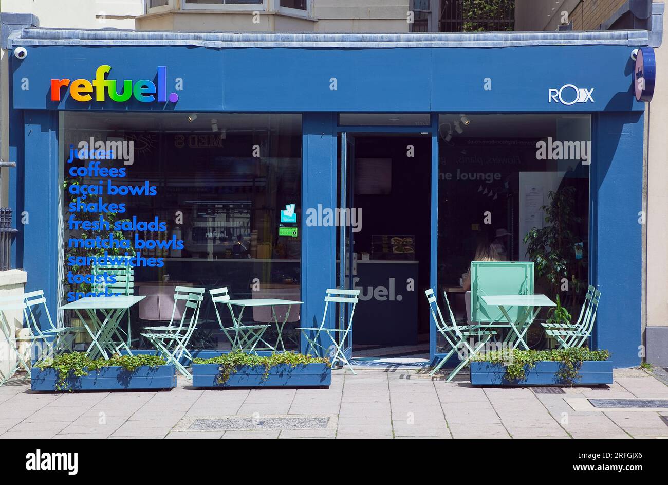 Inghilterra, East Sussex, Brighton, Hove, Western Road, Rifornisci una caffetteria sana con tavoli in metallo all'esterno. Foto Stock