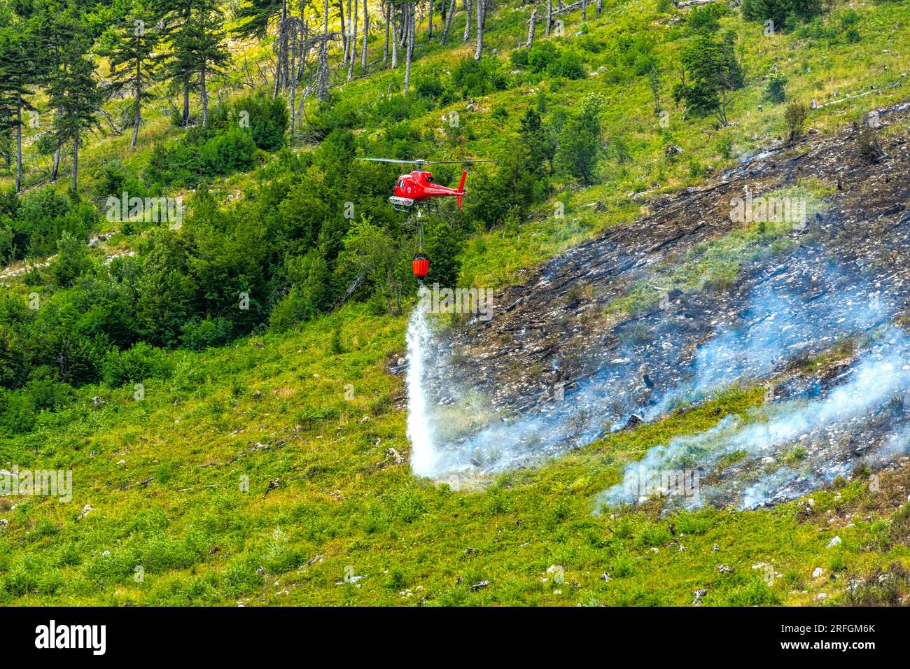 Scena drammatica con fiamme e fumo provenienti da un incendio boschivo. L'elicottero della protezione civile combatte le fiamme con l'acqua Monte Morrone, Parco Nazionale della Maiella Foto Stock