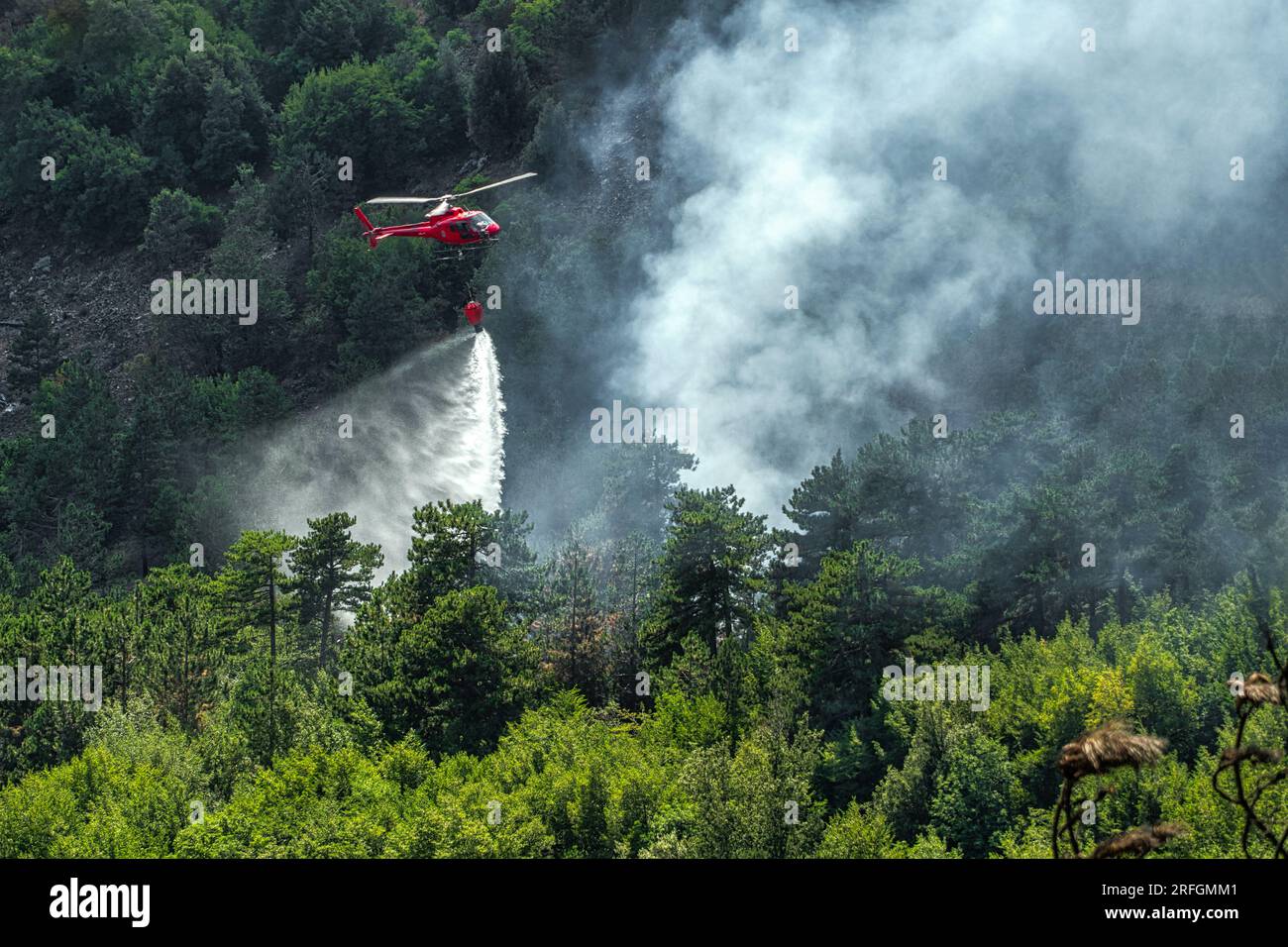 Scena drammatica con fiamme e fumo provenienti da un incendio boschivo. L'elicottero della protezione civile combatte le fiamme con l'acqua Monte Morrone, Parco Nazionale della Maiella Foto Stock