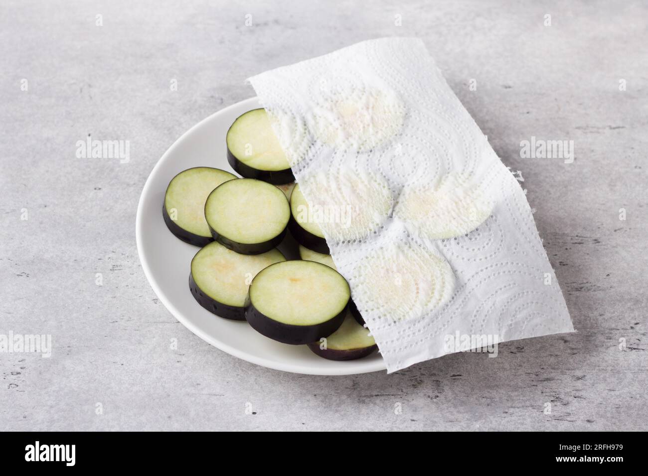 Essiccazione di fette di melanzane con un tovagliolo di carta su sfondo grigio testurizzato. Lavorazione delle melanzane prima della cottura, eliminando l'amaro. Foto Stock
