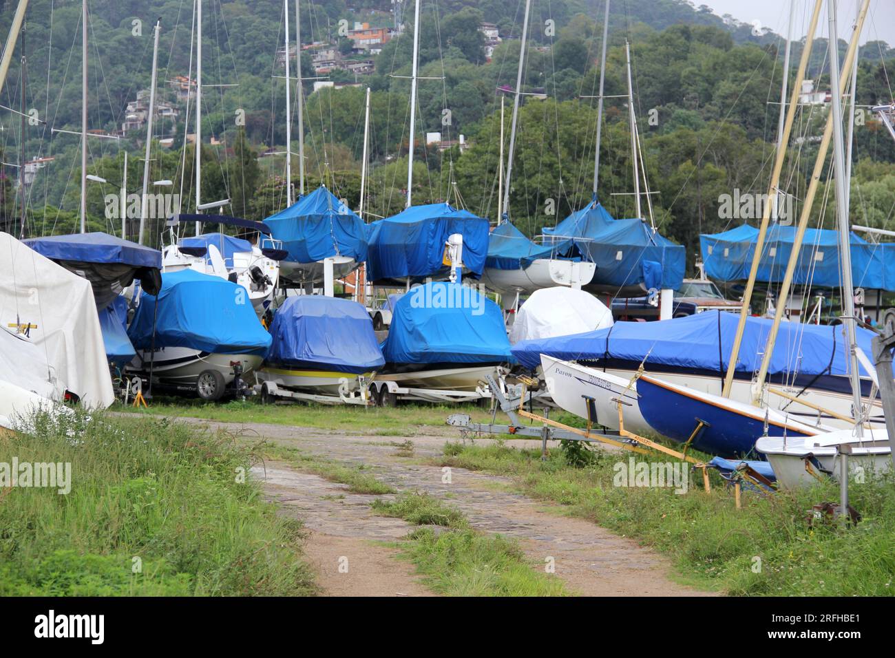 Parcheggio e imbarco di barche a vela, yacht, barche coperte di coperture blu, immagazzinate senza essere utilizzate nel lago o in mare Foto Stock